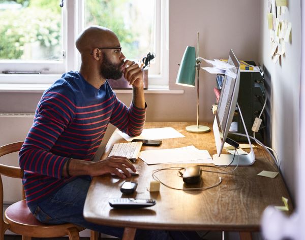 A man at home sitting studying at his desk with a computer.